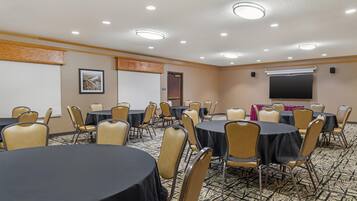 Un salón de conferencias con varias mesas y sillas, una pantalla de proyector y una pizarra.