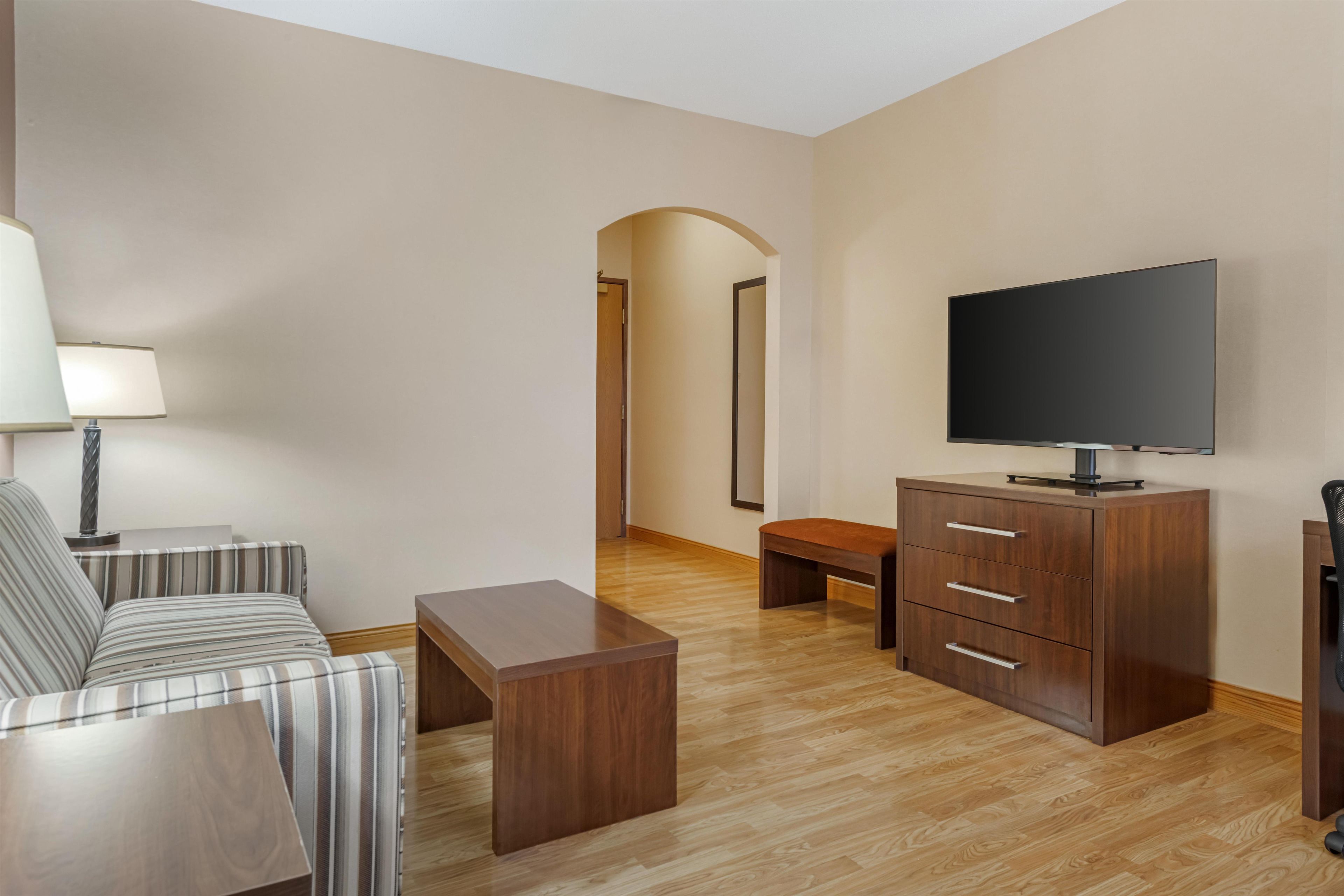 Ein Hotelzimmer mit einer Couch, einem Couchtisch, einem Fernseher, einem Holzschrank und einer Lampe.