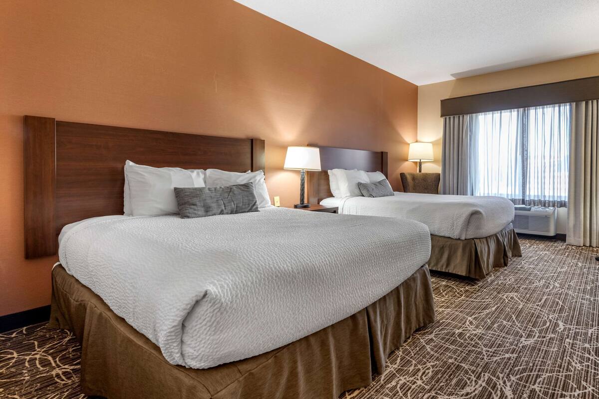 A hotel room with two beds, a large window with curtains, and a patterned carpet.