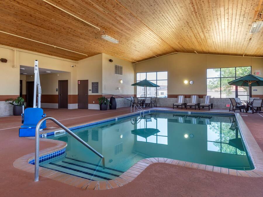 An indoor swimming pool with a wooden ceiling, lounge chairs, and a view of the outside.