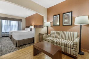 Una habitación de hotel con una cama, un sofá, una mesa de centro y dos lámparas.
