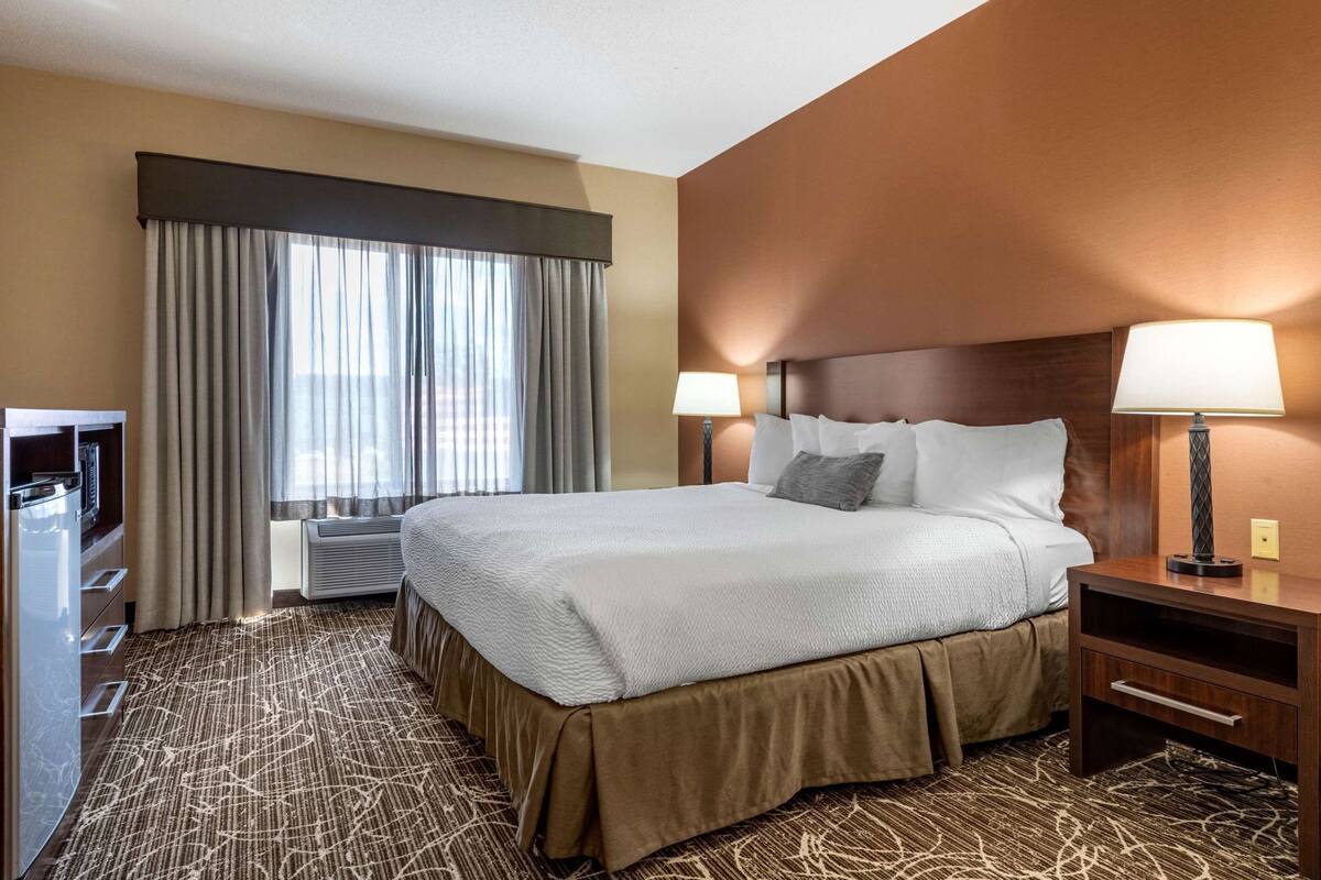 A hotel room with a large bed, two bedside lamps, a TV, and a window with curtains.