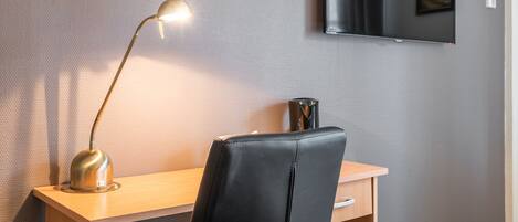 Una habitación de hotel moderna con un escritorio de madera, una silla de cuero negro, una lámpara de escritorio y un televisor de pantalla plana montado en la pared.