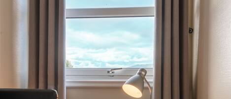 Una habitación pequeña con escritorio, silla y ventana con cortinas.