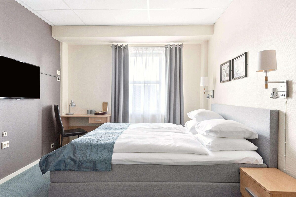 Hotelkamer met een bed, een bureau, een stoel, een televisie en een raam met gordijnen.