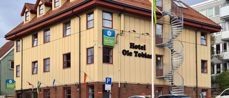 Un hotel de varios pisos con fachada amarilla, un cartel que dice 'Hotel Ole Tobias' y un letrero de estacionamiento que indica una zona de aparcamiento.