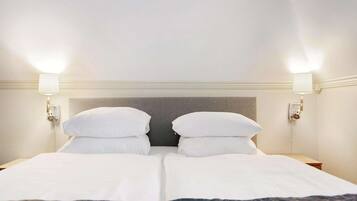 Habitación de hotel con cama doble, dos lámparas de noche y cabecera en tonos neutros.