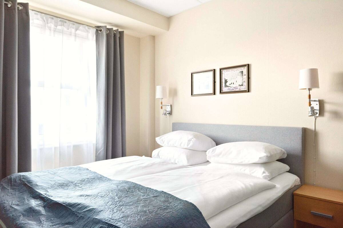 Une chambre d’hôtel avec un lit, une table de chevet, une lampe et deux tableaux encadrés au mur.