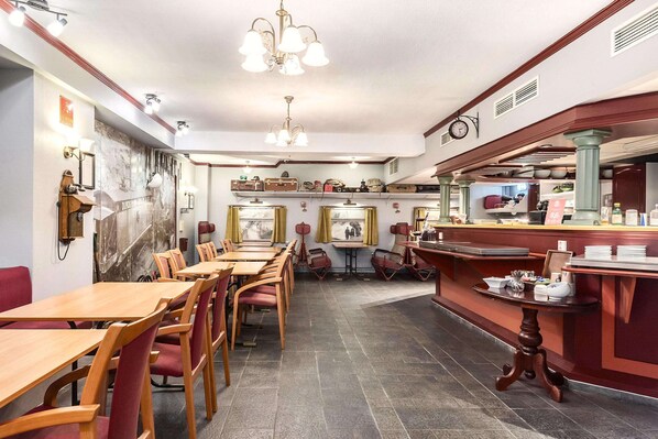 Interior de restaurante con mesas y sillas de madera, una zona de bar y un reloj colgado en la pared.