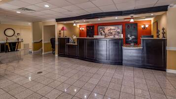A hotel reception area with a tiled floor, a reception desk, a chair, and a wall-mounted lamp.