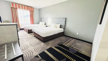 A hotel room with two beds, a desk, and a view of the city.