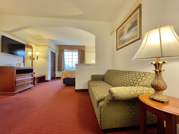 A hotel room with a sofa, a TV, a lamp, a dresser, and a bed.