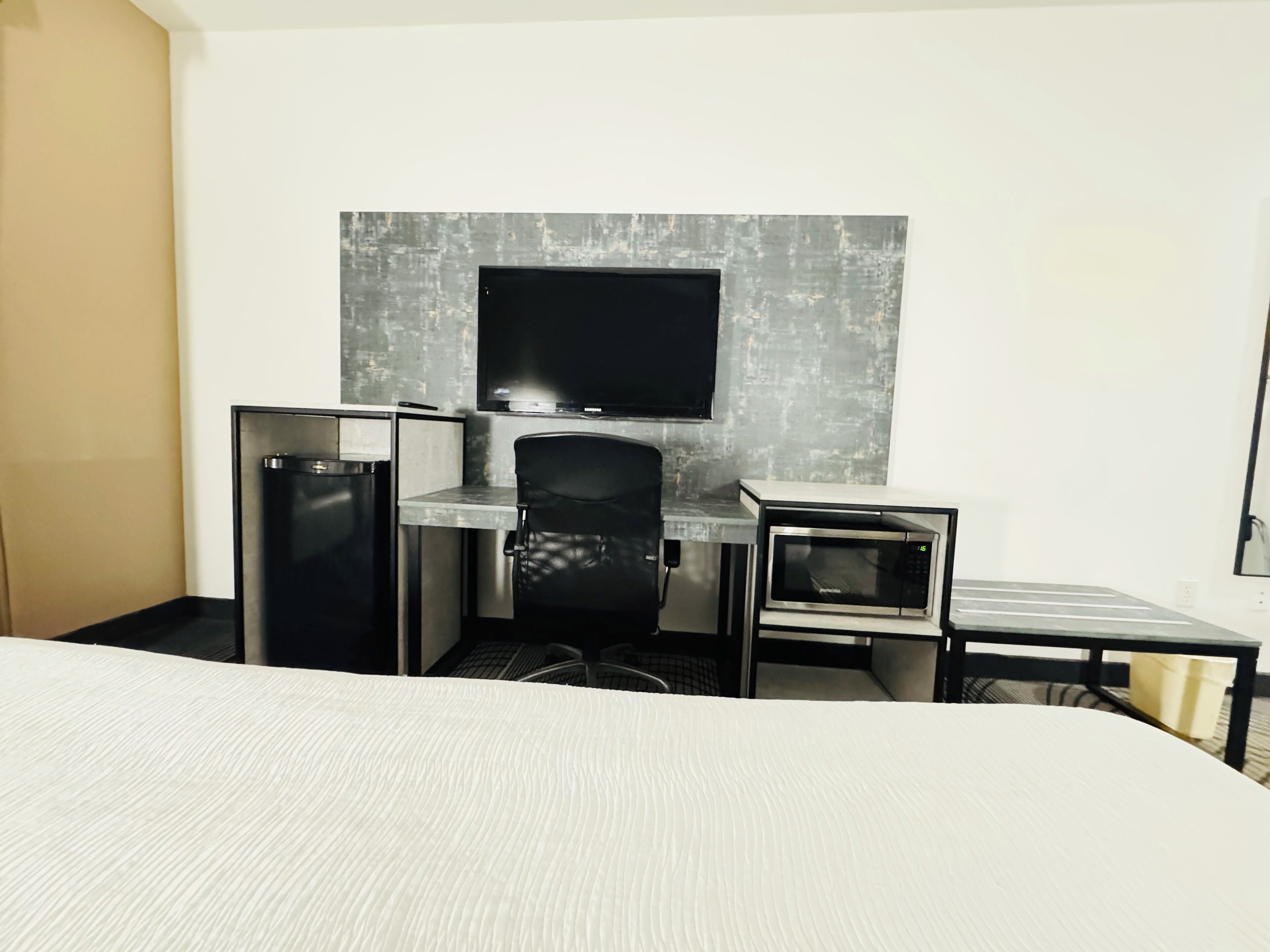 A hotel room with a bed, a desk, a chair, a television, and a microwave.