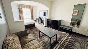 Une chambre d’hôtel comprenant un lit, un canapé, un bureau, un miroir et une kitchenette.