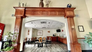 Un hall d’hôtel doté d’un comptoir d’accueil en bois, de plusieurs espaces aménagés avec des sièges et d’un sol carrelé.