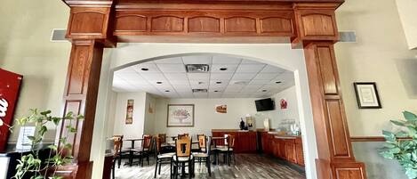 A hotel lobby with a wooden reception desk, multiple seating areas, and a tiled floor.