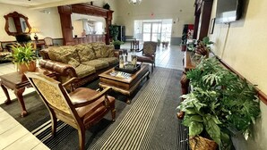 Un hall d’entrée spacieux, avec un canapé en cuir, un fauteuil en bois, une table basse et une grande plante en pot.