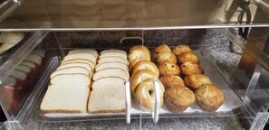A bakery display case with various baked goods including bread, bagels, and muffins.