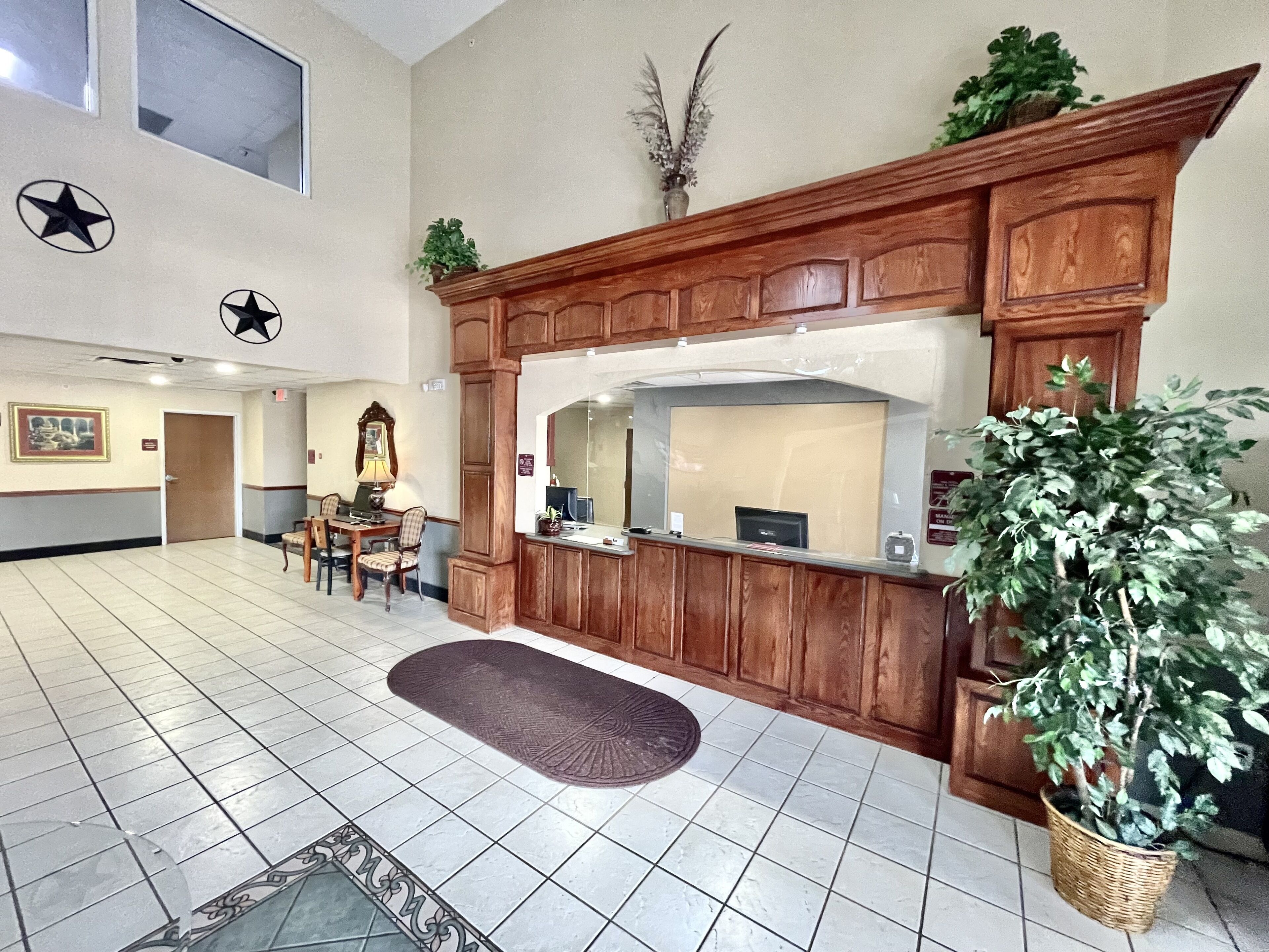 A reception area with a wooden reception desk, a large mirror, a potted plant, and a tiled floor.