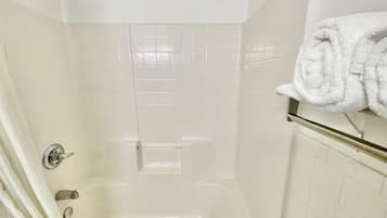 Une douche carrelée de carreaux blancs, dotée d’une porte en verre, d’un porte-serviettes et d’un panneau de commande.