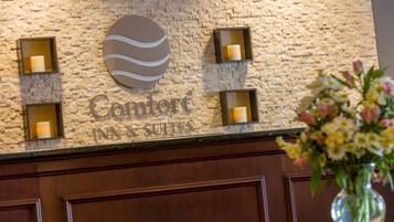 A stone wall with the Comfort Inn & Suites sign, four wall-mounted candles, and a vase of flowers.
