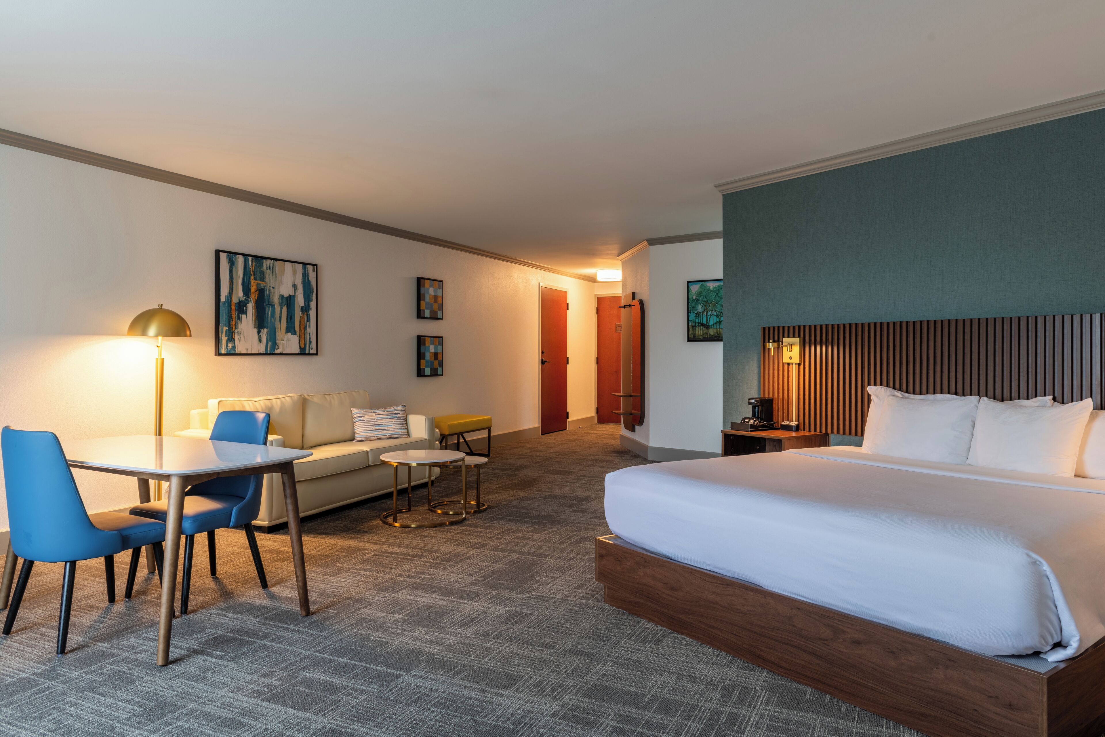 Una habitación de hotel con una cama grande, un escritorio con dos sillas, un sofá y una mesita.