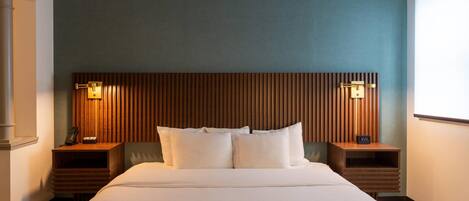 A hotel room with a large bed, two bedside tables with lamps, a wooden headboard, and a view of the outdoors.