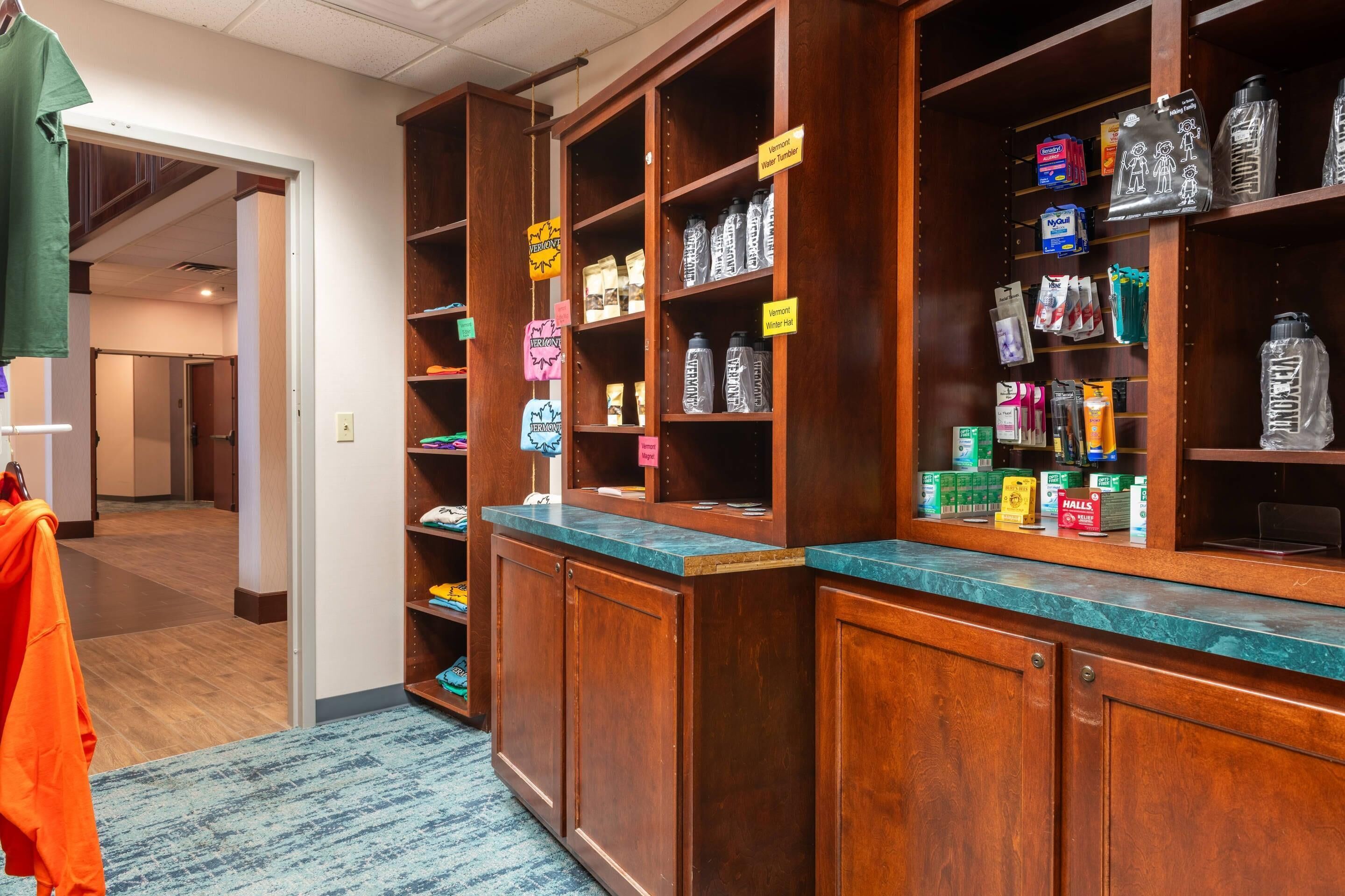 A hotel lobby with wooden reception desks, shelves stocked with toiletries, and a carpeted floor.