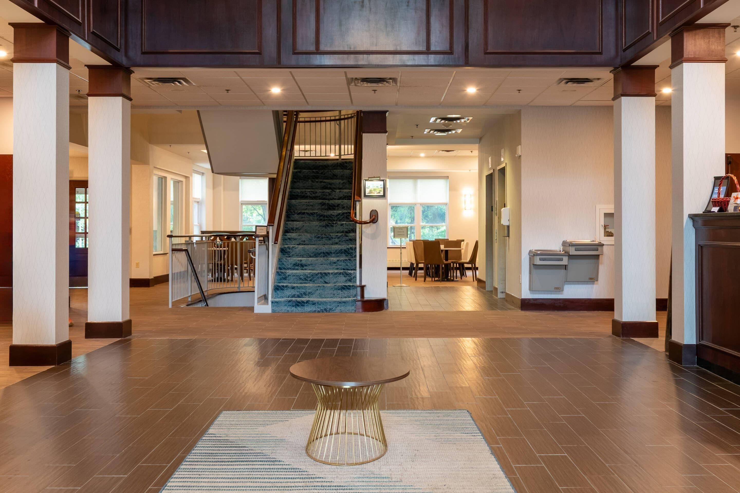 A spacious lobby with a central staircase, a reception desk, and a seating area.