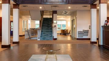 A spacious lobby with a central staircase, a reception desk, and a seating area.