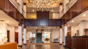 A spacious lobby with a grand staircase, a reception desk, and a chandelier. - Comfort Inn & Suites Near Burke Mountain (St. Johnsbury)
