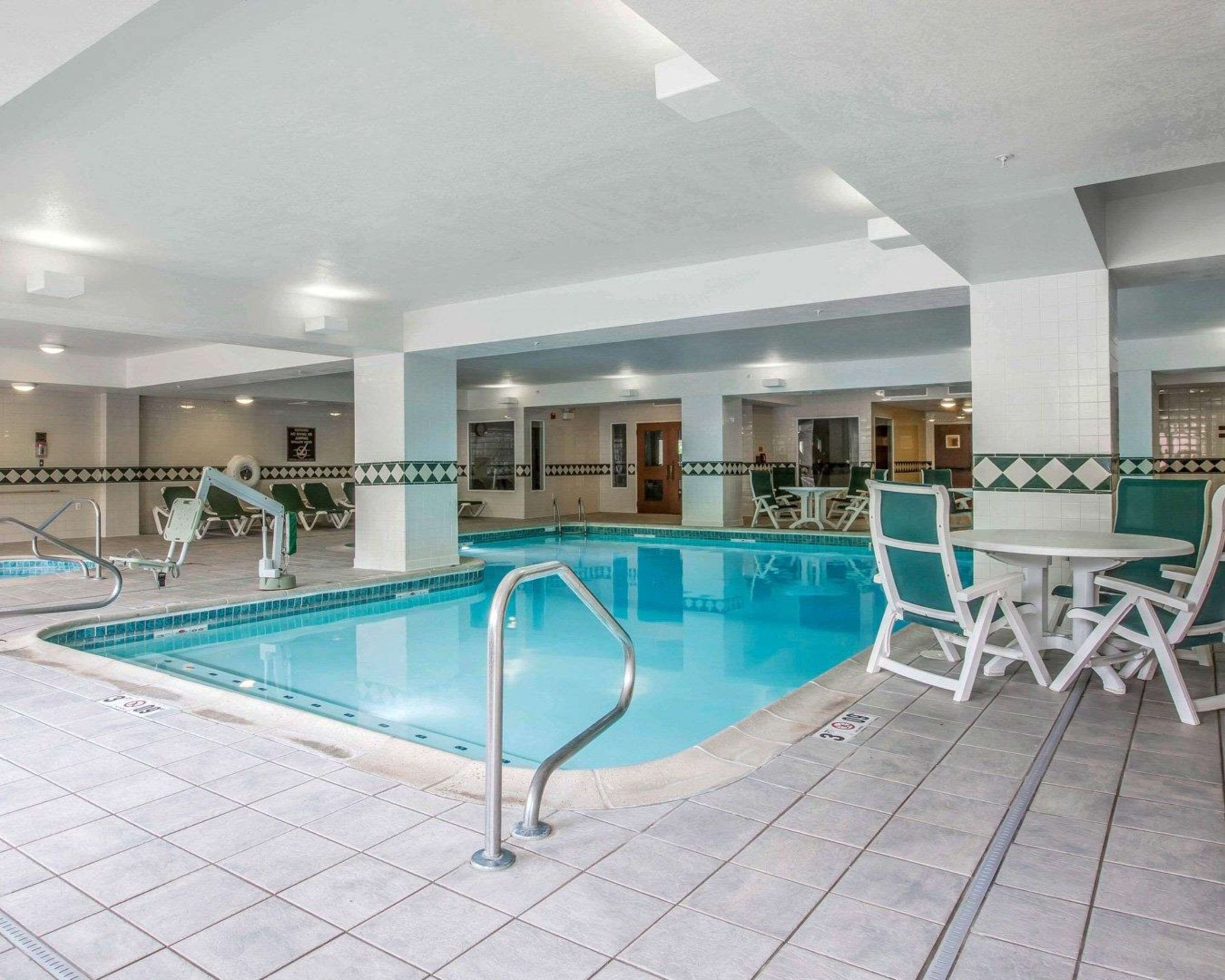 Una piscina interior con suelo de baldosas, sillas junto a la piscina y una mesa con sillas.