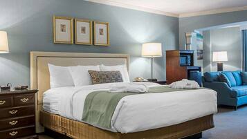 A hotel room with a large bed, a dresser, a blue sofa, and framed pictures on the wall.