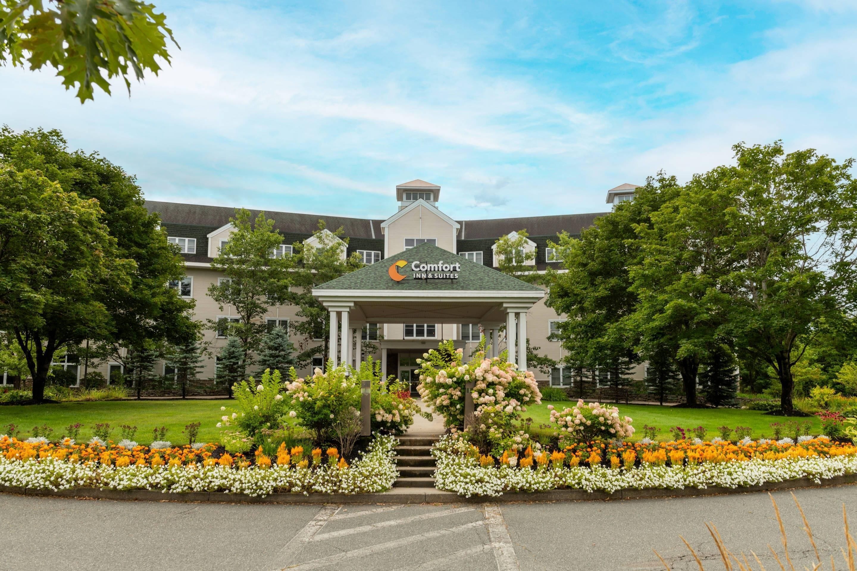 A hotel entrance with a central archway, surrounded by a flower bed with various colors.