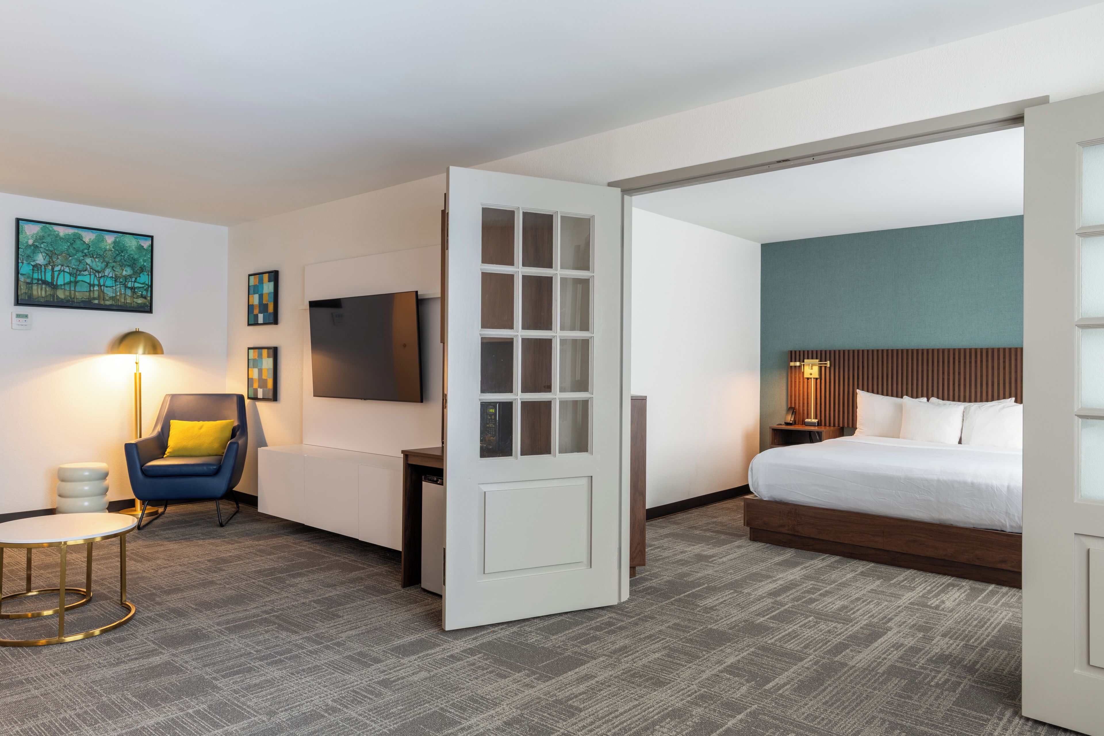 A hotel room with a bed, a desk, a chair, a TV, and a door.