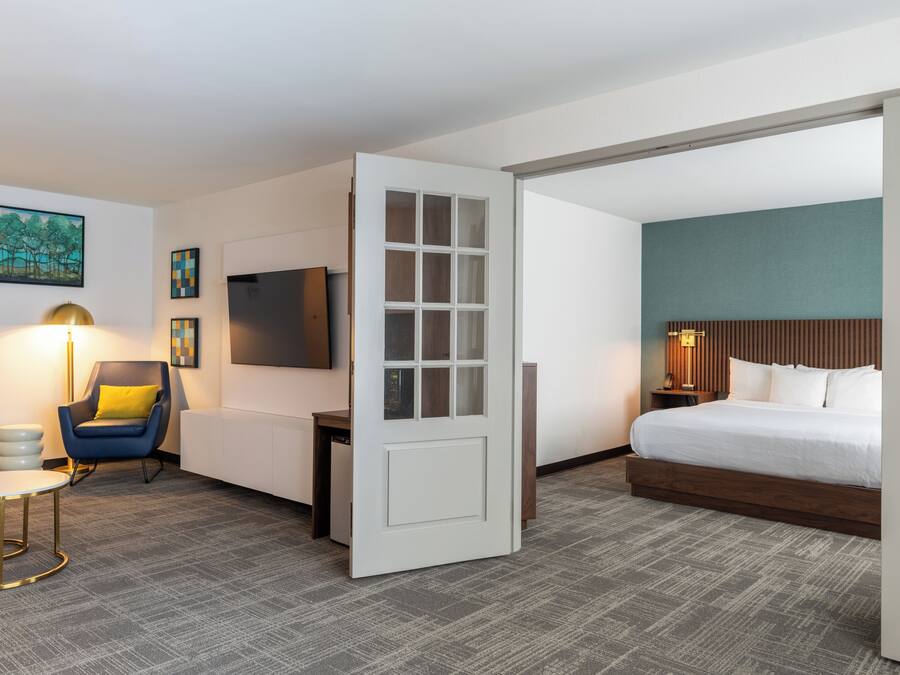 A hotel room with a bed, a desk, a chair, a TV, and a door.