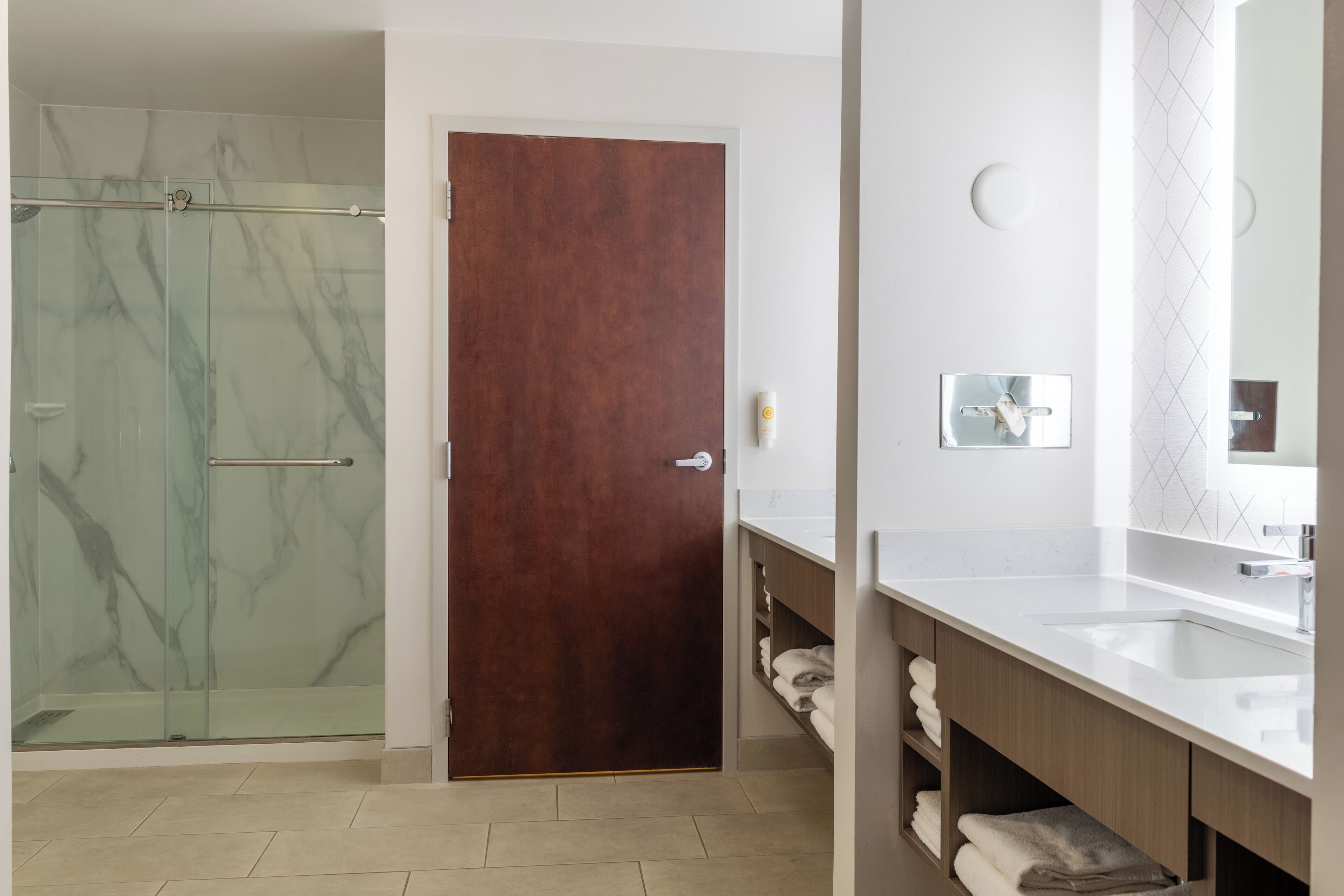 Un baño moderno con ducha de vidrio, puerta de madera y tocador blanco con espejo.