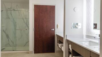 Un baño moderno con ducha de vidrio, puerta de madera y tocador blanco con espejo.