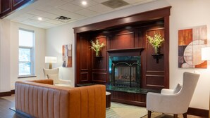 A modern living room with a fireplace, leather sofa, armchair, and a large window. - Comfort Inn & Suites Near Burke Mountain (St. Johnsbury)
