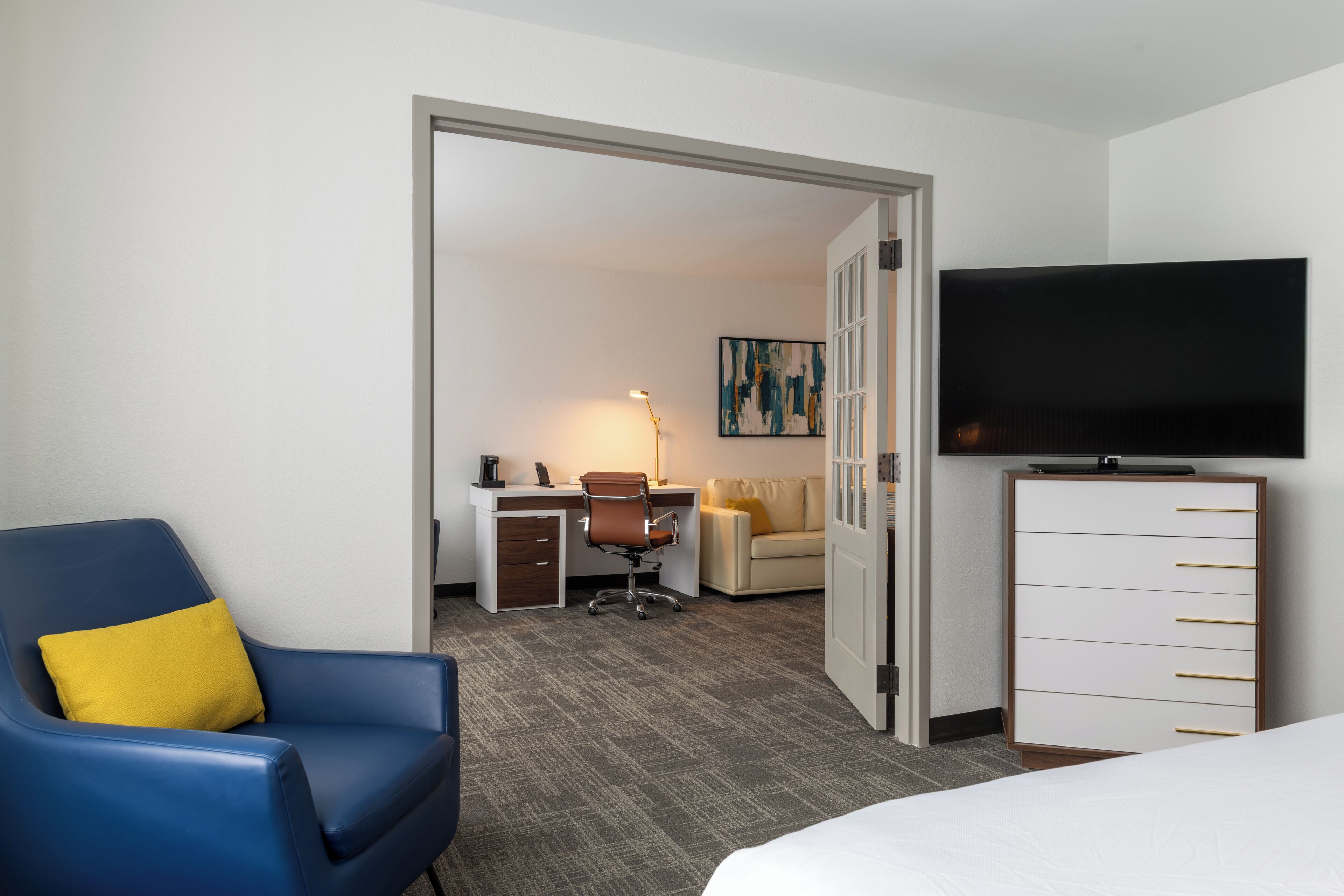 A hotel room with a bed, a desk with a chair, a television, and a wardrobe.