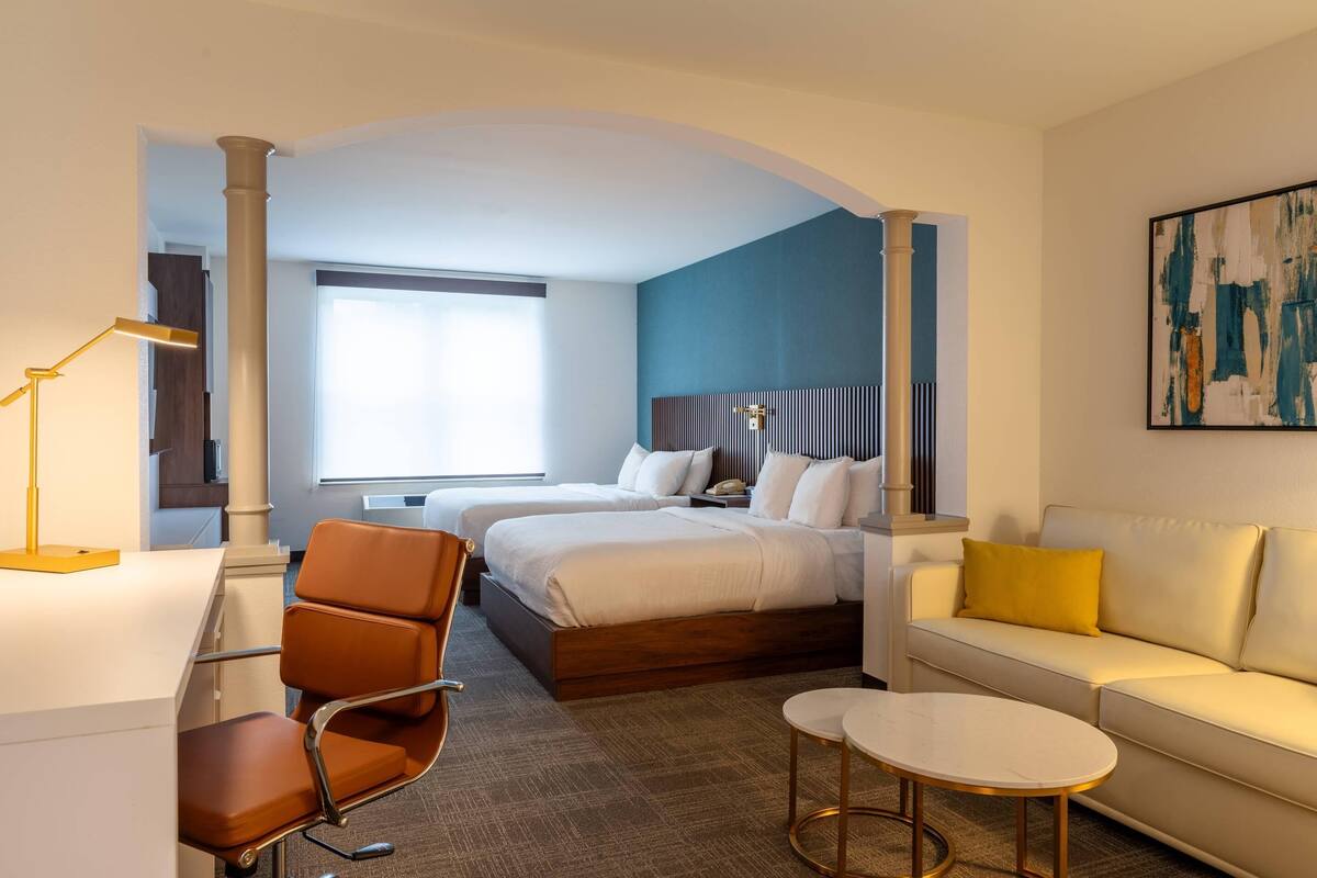 Une chambre d’hôtel avec deux lits, un bureau, une chaise, un canapé et une petite table.