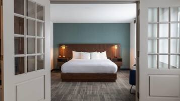 A hotel room with a large bed, two bedside tables with lamps, a wooden headboard, and a carpeted floor.