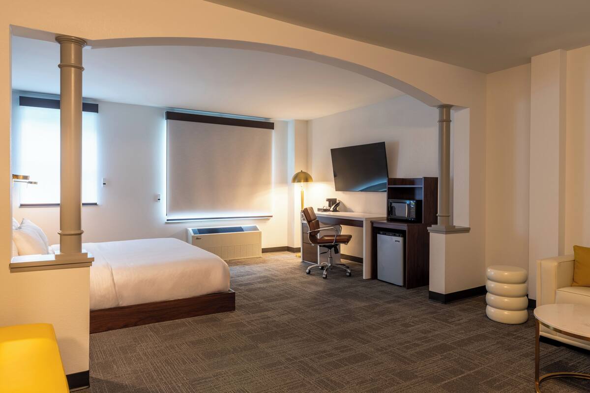 Une chambre d’hôtel comprenant un lit, un bureau, une chaise, une télévision et un petit coin salon.