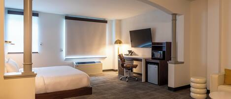 A hotel room with a bed, desk, chair, TV, and a small seating area.