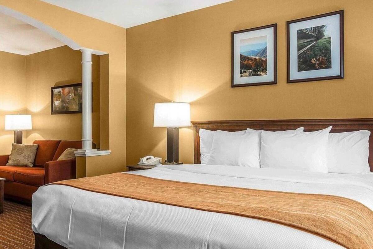 Une chambre d’hôtel avec un grand lit, deux lampes de chevet, une table de chevet, une chaise et deux tableaux encadrés au mur.