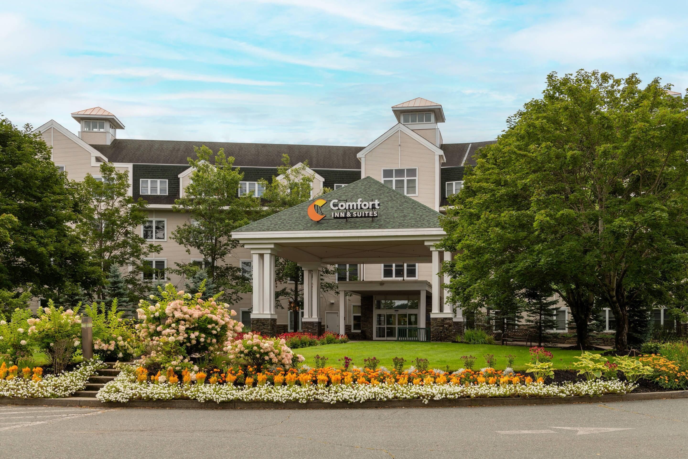 A hotel with a covered entrance, multiple floors, and a landscaped garden with various flowers.