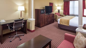 Camera d'albergo con scrivania, sedia, televisore, comò, letto e un piccolo tavolino.