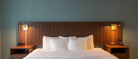 A hotel room with a large bed, two bedside tables, a wooden headboard, and two wall-mounted lamps.