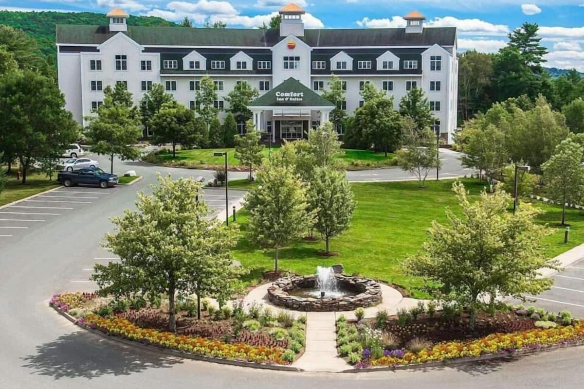 Un grand hôtel blanc, doté d’une entrée centrale, entouré d’une pelouse bien entretenue et d’un jardin circulaire agrémenté d’une fontaine.