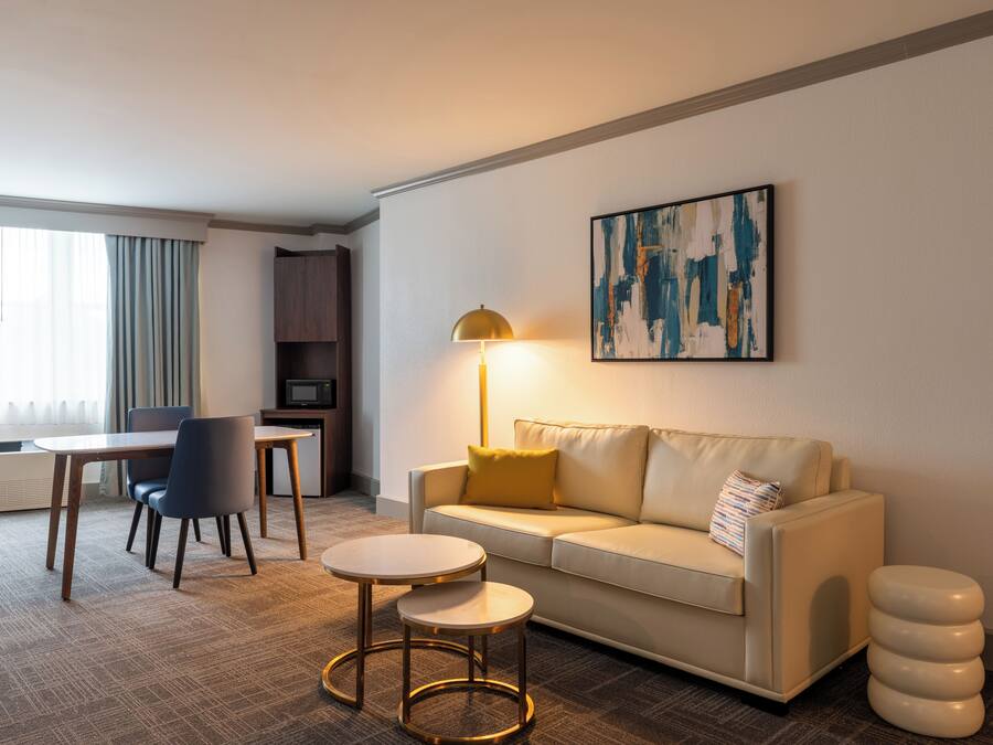 Une chambre d’hôtel moderne avec un canapé, deux tables rondes, une lampe et un tableau au mur.